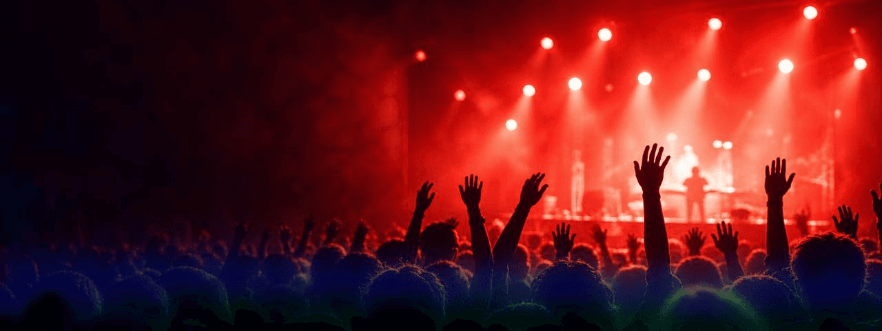Crowd with raised hands at a concert under red stage lights